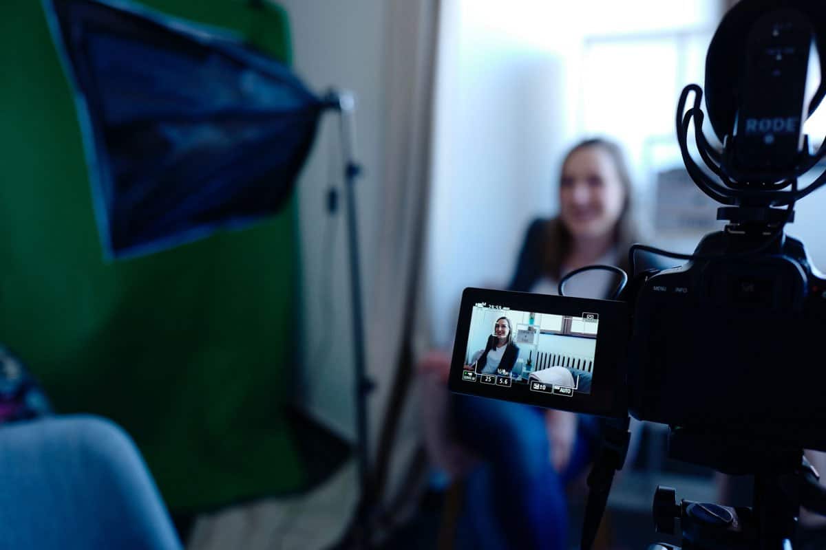 A woman in front of a camera and lights, recording her vlog.