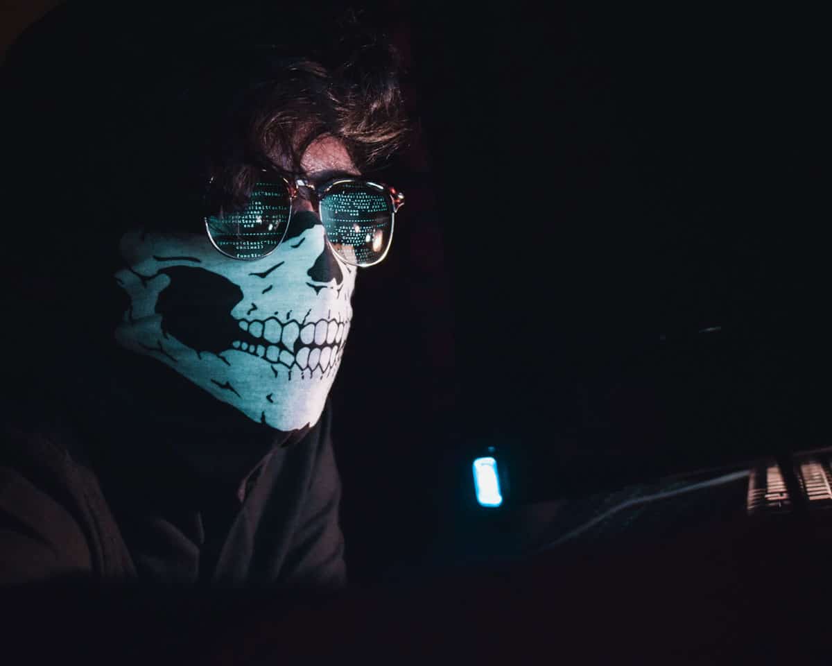 A computer hacker with a skull face mask, reading computer code