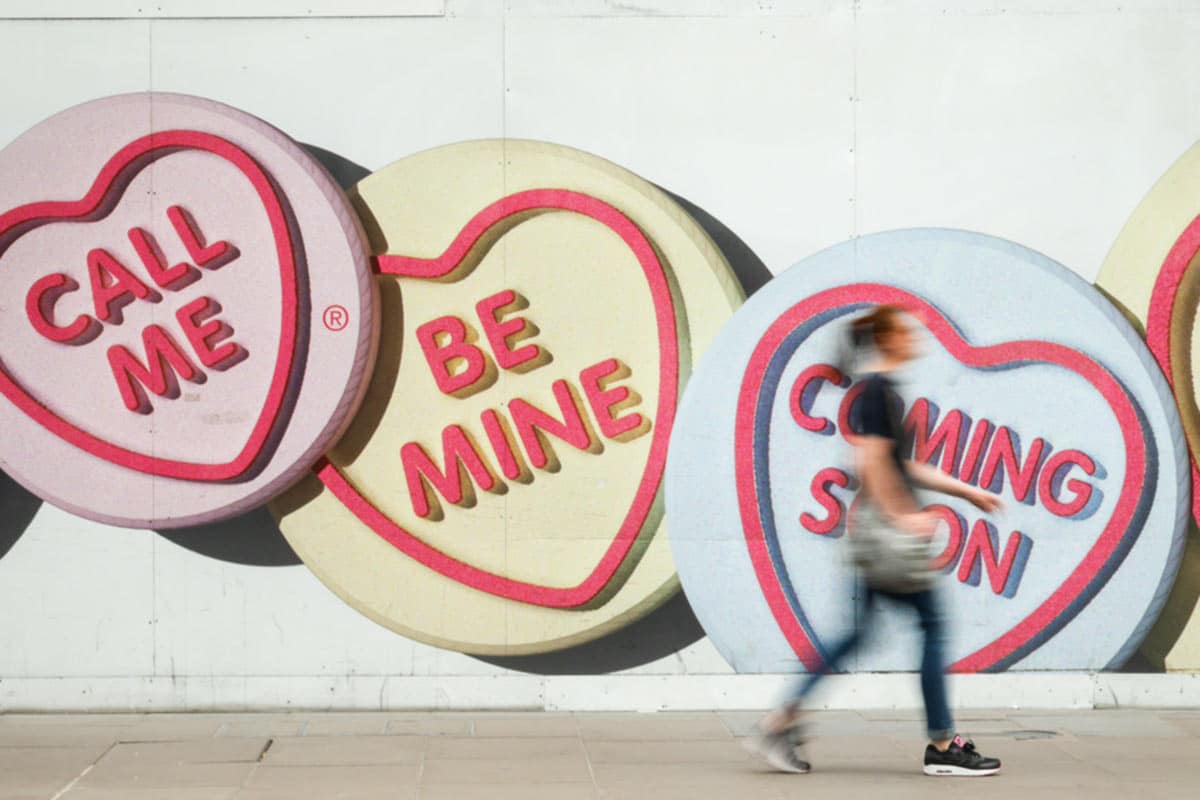 Woman walking in front of candy hearts painted on a wall.