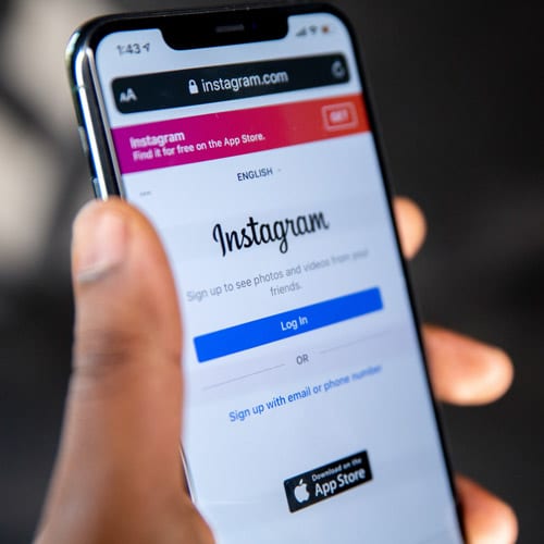 A man holding a smart phone, looking at a signup page for the social media platform Instagram